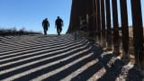U.S. Customs and Border Protection personnel walk along a section of fence at the U.S.-Mexico border.