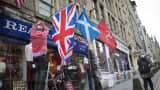 A shopkeeper erects a British Union flag next to Scottish Saltire flag as he prepares the front of his store for business