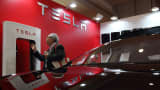 A man looks at a battery charger near a Tesla Motors Model S electric vehicle.