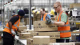 Employees collect packaged customer orders from a conveyor belt ahead of shipping at one of Amazon.com Inc.'s fulfillment centers in Rugeley, U.K.