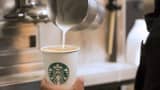 A barista pours milk into a cup of coffee at a Starbucks store.