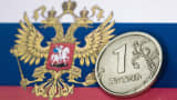 A Russian one Ruble coin is shown on the Russian flag.