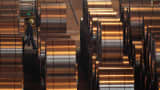 A worker walks among coils of galvanized steel at a steel factory.