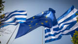 The national flag of Greece and the flag of the European Union fly above a government building in Athens.