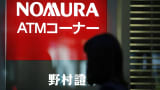 A pedestrian walks past illuminated signage for Nomura Securities Co., a unit of Nomura Holdings Inc in Tokyo, Japan.