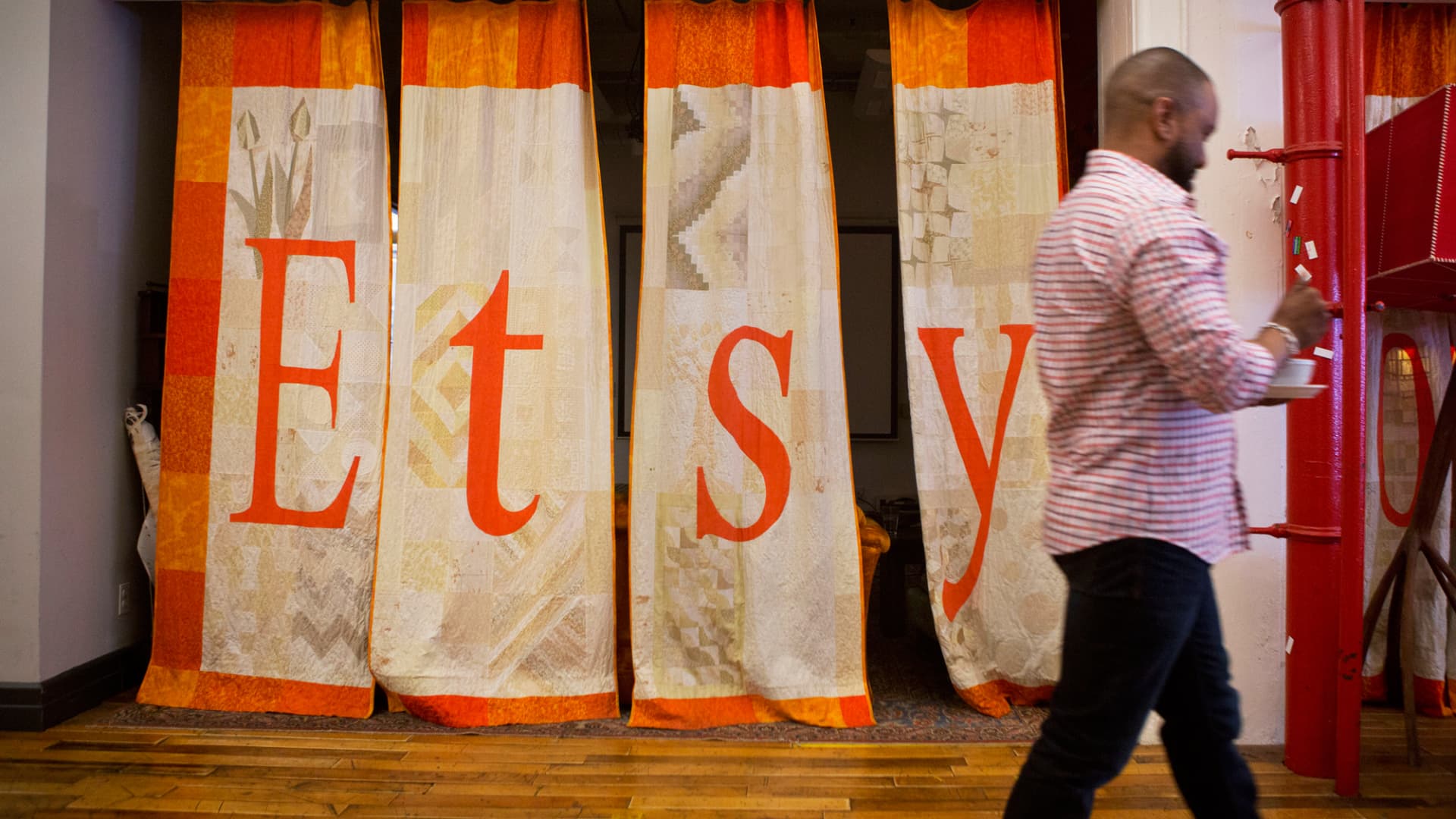 An employee walks past a quilt displaying Etsy signage at the company's headquarters in Brooklyn, New York.