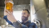 Brewery worker examining beer in beaker. Craft breweries continue to grow.