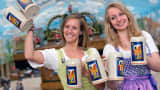 Women wearing the traditional Bavarian Dirndls present the offical Oktoberfest beer mugs at the Oktoberfest grounds in Munich, southern Germany, on August 18, 2015.