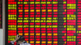 A man stands in front of an electronic board displaying share prices at a securities exchange house in Shanghai, China.