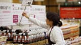 An employee places a new price sign on bottles of coffee at an Aeon Co. supermarket in Chiba, Japan.