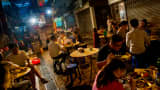 A large group of people sit around small tables in an alleyway in Hong Kong to enjoy their street food dinner