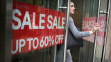 Sale signs are displayed as a shopper exits a store on 34th Street in New York.