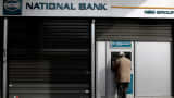 A man withdraws cash from an ATM outside a National Bank branch in Athens.