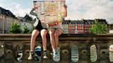 Two teenage girls sitting on bridge holding city map in front of them, in Copenhagen.