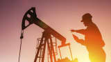 A worker stands in front of an oil drill at sunset.
