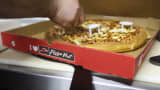 An employee places plastic box supports around a freshly cooked pizza as he prepares a takeaway order for a customer, in the kitchen of a Pizza Hut restaurant, owned by Yum! Brands Inc.