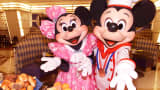 Mickey Mouse in chef's uniform, accompanied by Minnie Mouse, display a heap of breads on a plate
