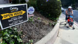 A woman pushes a child in a stroller past property for sale sign in Monterey Park, California.