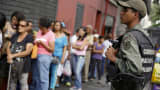 A Venezuelan soldier stands guard next to people forming a line to try to buy cornmeal flour and margarine at a pharmacy in Caracas March 15, 2016.