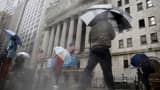Pedestrians carry umbrellas while walking past the New York Stock Exchange.
