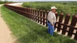 Farmer Fausto Salinas stands along the border fence, in McAllen, Texas.