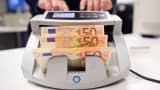 A worker puts 50 euro bank notes into a counting machine.