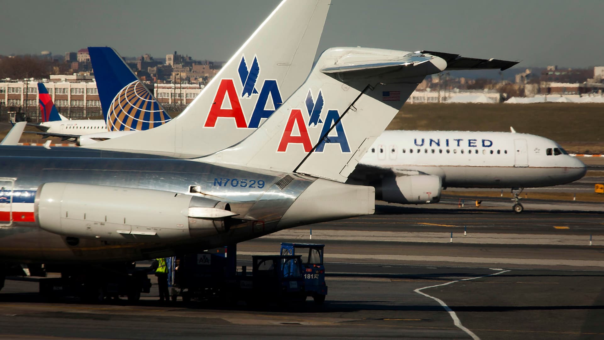 An American Airlines Inc. McDonnell Douglas MD-82 plane sits parked at a gate while a United Continental Holdings plane taxis down the runway at LaGuardia Airport in the Queens borough of New York.