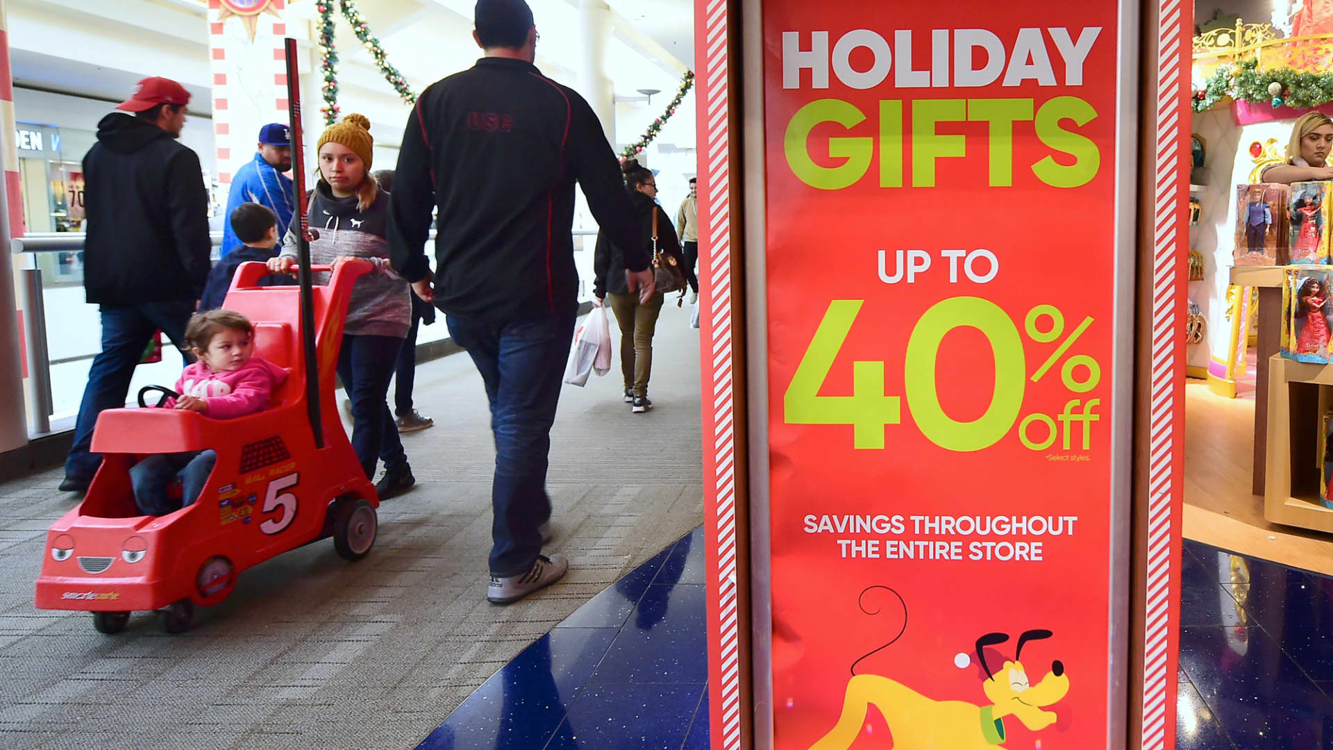 Christmas week shoppers walk past signs offering sales at a Montebello shopping mall in Montebello, California on December 22, 2016.