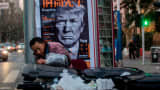 This picture taken on March 2, 2017 shows a man searching rubbish bins in front of an news stand advertising a Chinese newspaper with the front page photo of U.S. President Donald Trump.