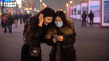 Chinese women look at their mobile phone as they walk in a shopping area in Beijing.