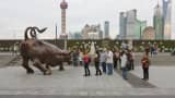 Tourists watching the bull statue in front of the Stock Exchange on the Bund, Pudong skyline in the distance, Shanghai, China.