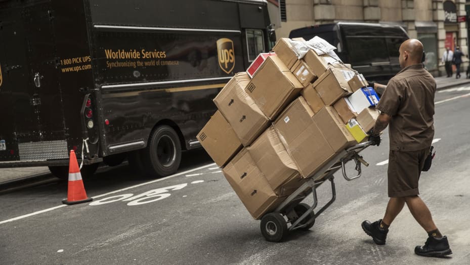 United Parcel Service (UPS) driver pushes a dolly of packages towards a delivery van on a street in New York.