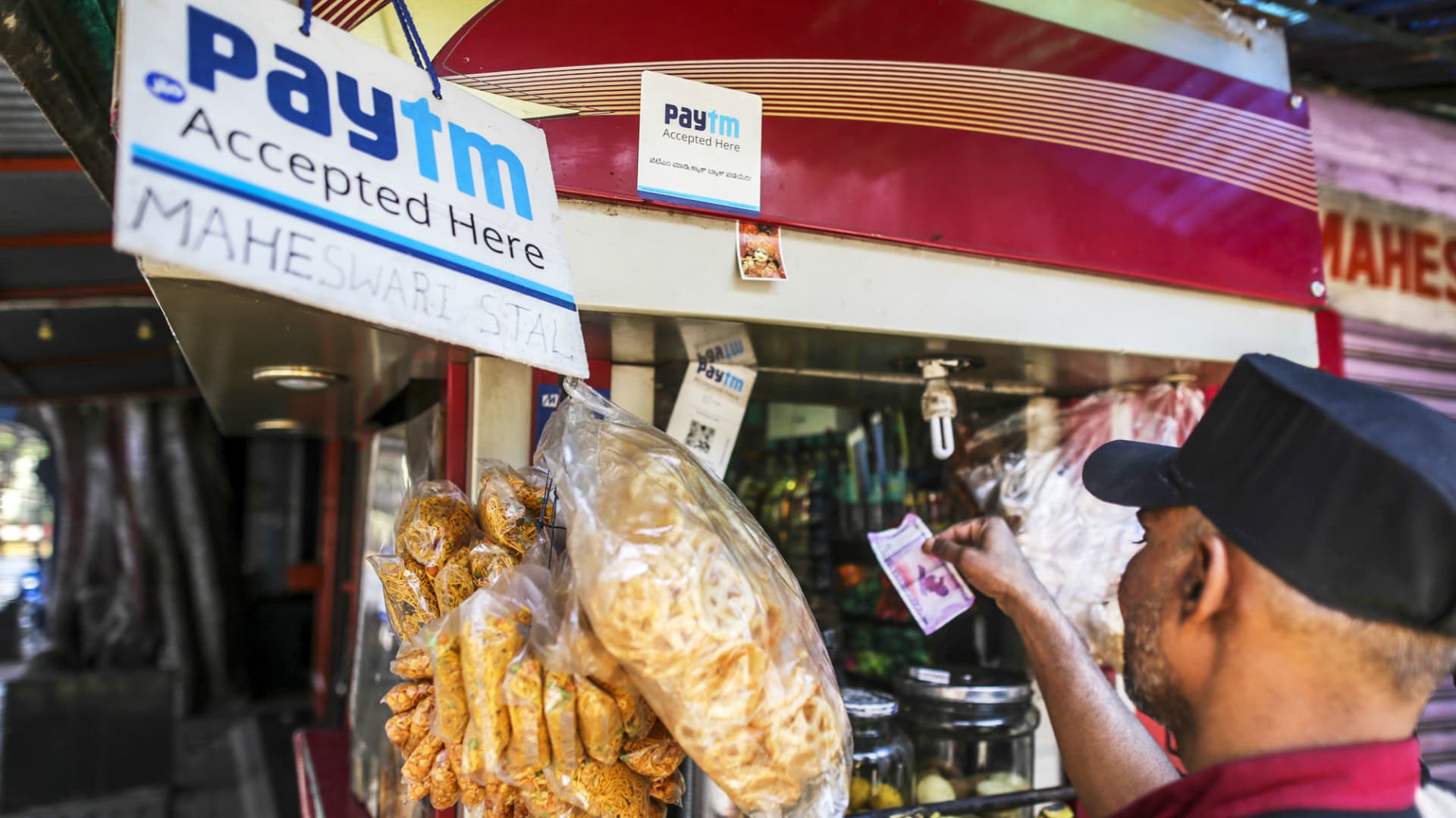 A customer uses an Indian Rupee banknote to pay for a purchase as a sign for PayTM online payment method is displayed at a stall selling snacks in Bengaluru, India.