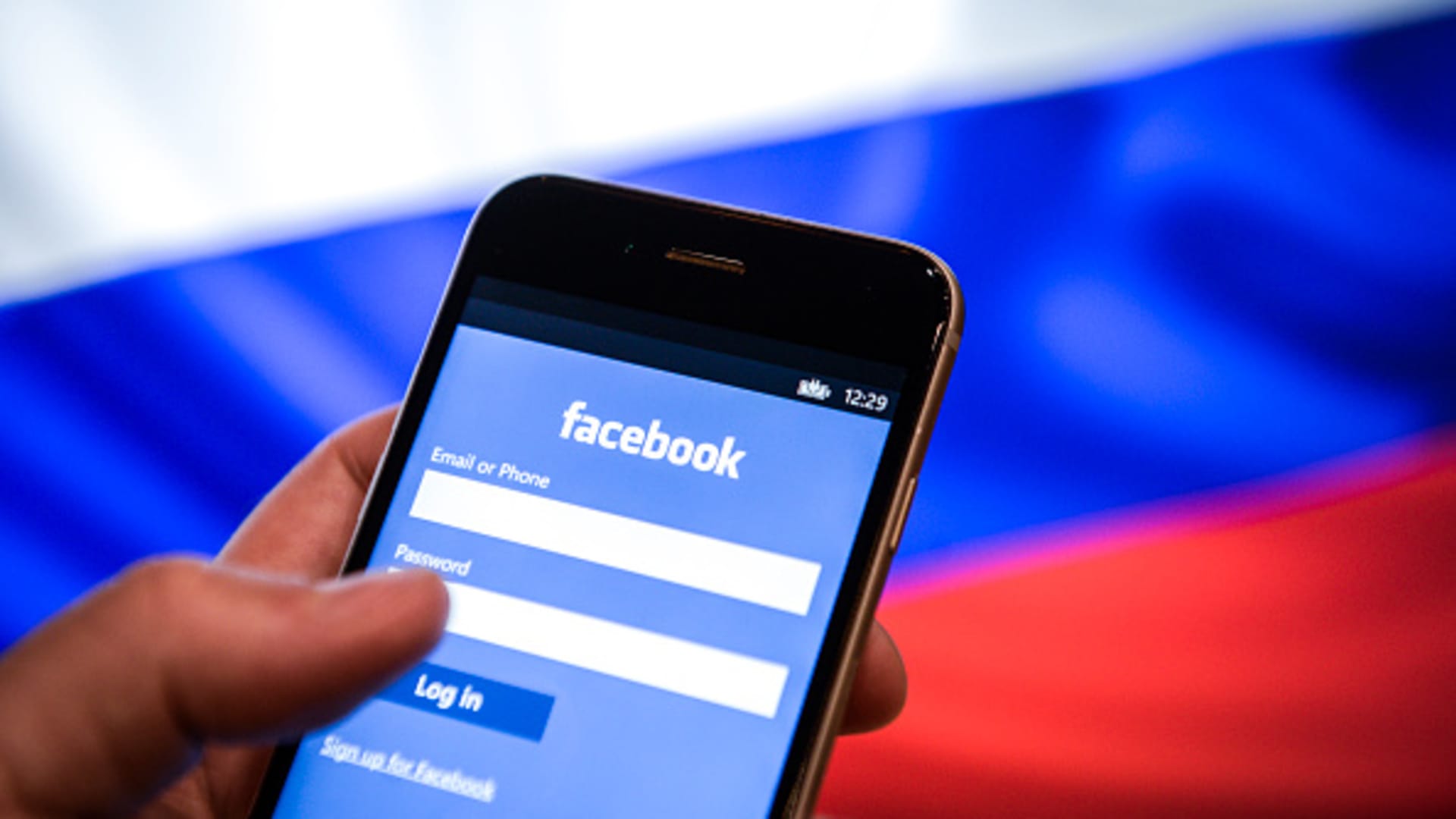 An iPhone with a Facebook logo is seen with a Russian flag in the background in this photo illustration.