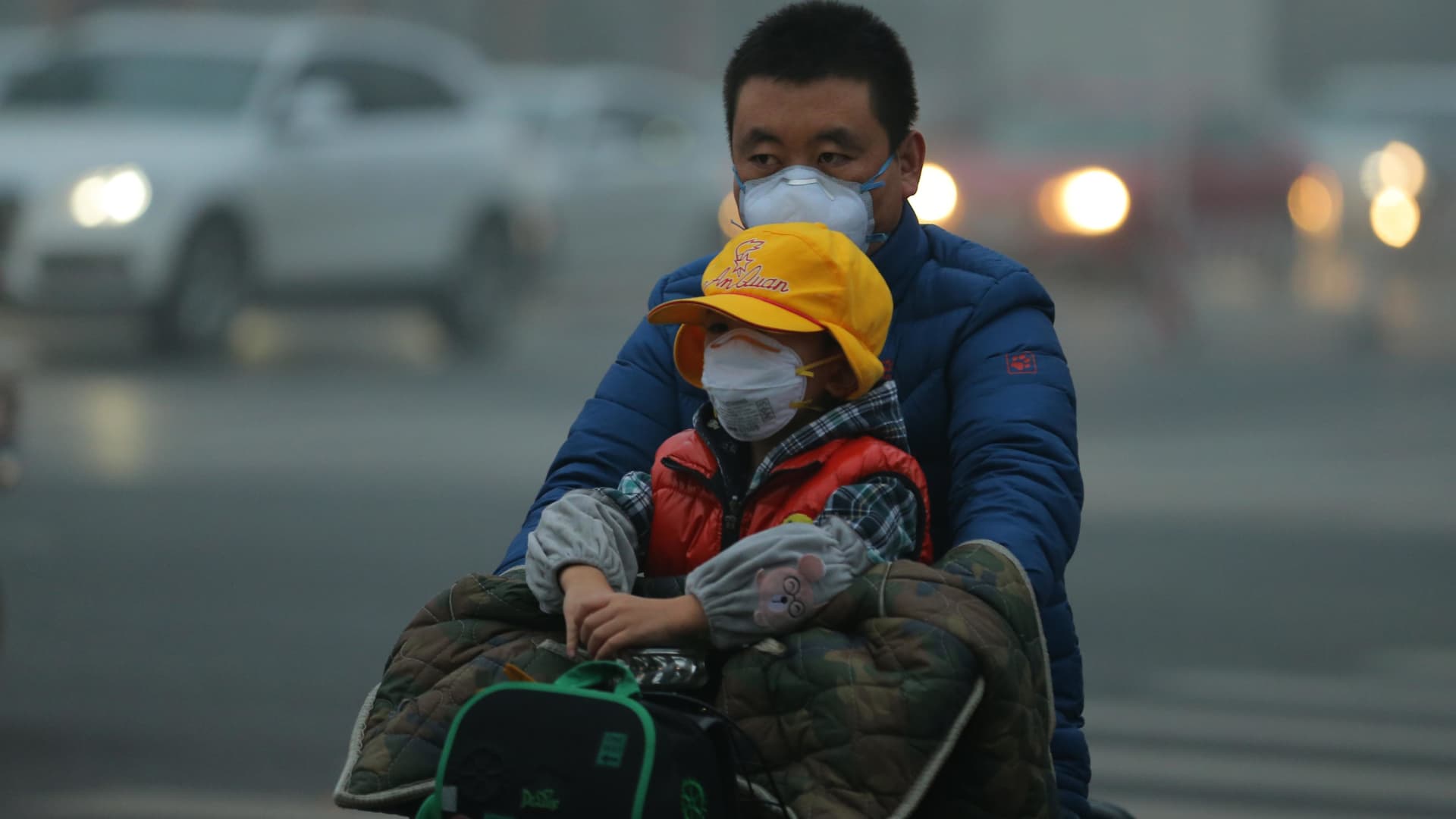 A man and a child wearing breathing masks are seen on an electric vehicle in smog on November 14, 2018 in Beijing, China.
