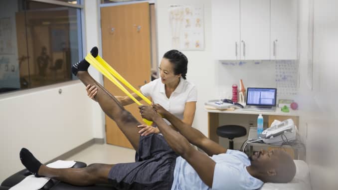 GP: Physical therapist guiding patient using resistance band leg