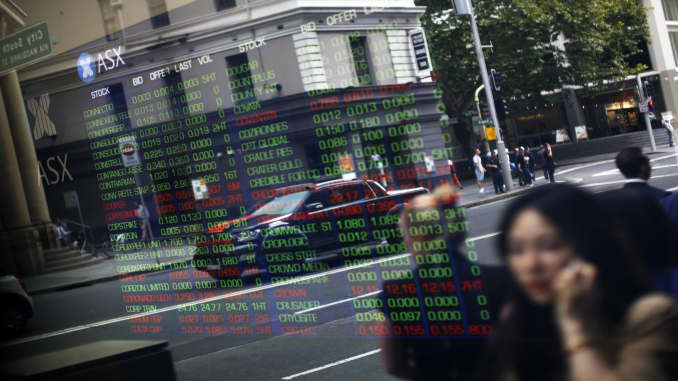 Pedestrians are reflected in a window as they walk past an electronic stock board at the ASX Ltd. exchange centre in Sydney, Australia, on Thursday, Feb. 14, 2019.