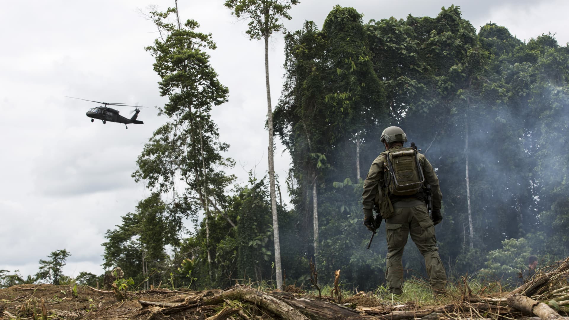 An anti-narcotics police officer stands as a police helicopter flies over a coca field during an operation in Tumaco, Narino department, Colombia, on Tuesday, May 8, 2019.