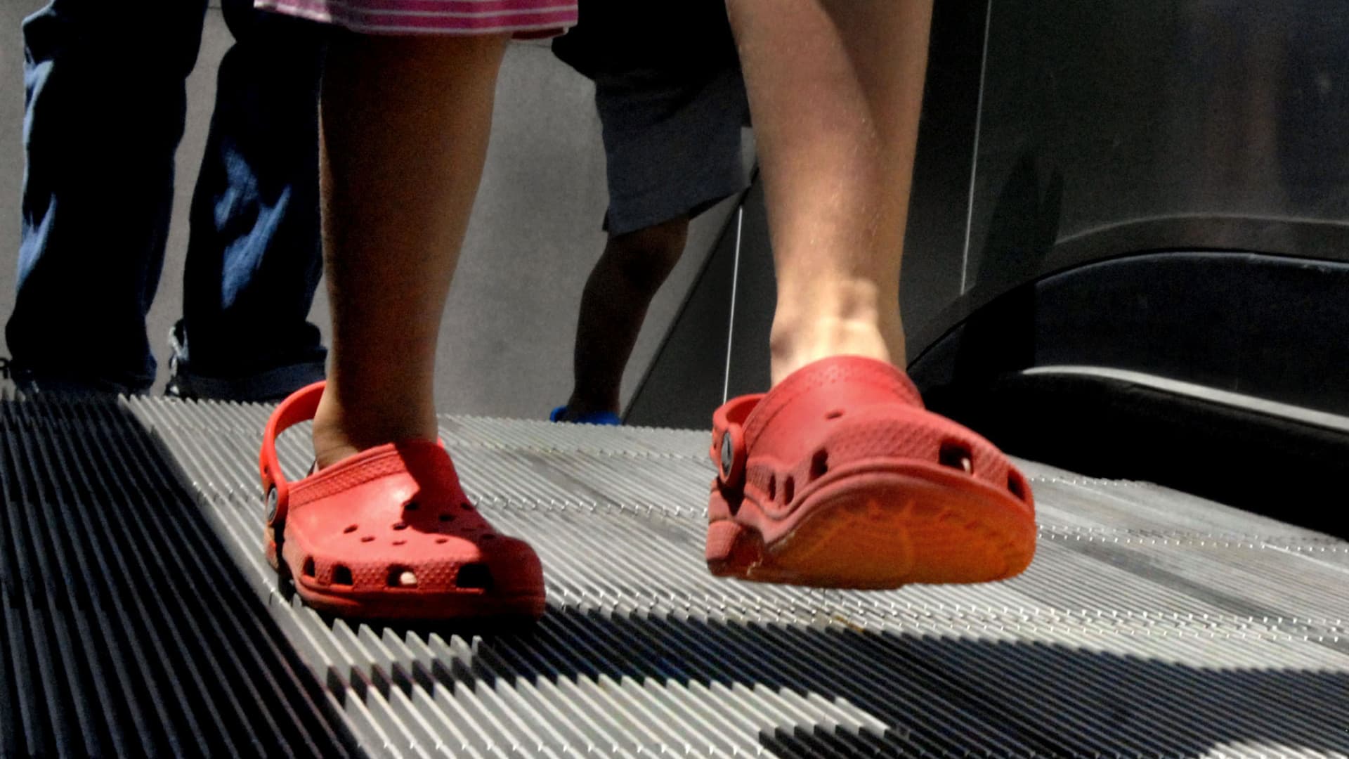A kid wears Crocs on an escalator.