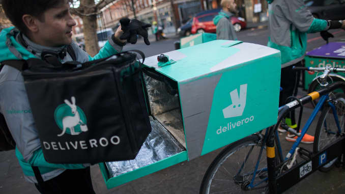 A food delivery courier places a bag of food into the back of his bicycle as he prepares to deliver an order from Deliveroo in London.