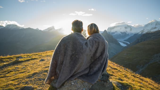 Couple huddle in blanket, watch mountain sunrise