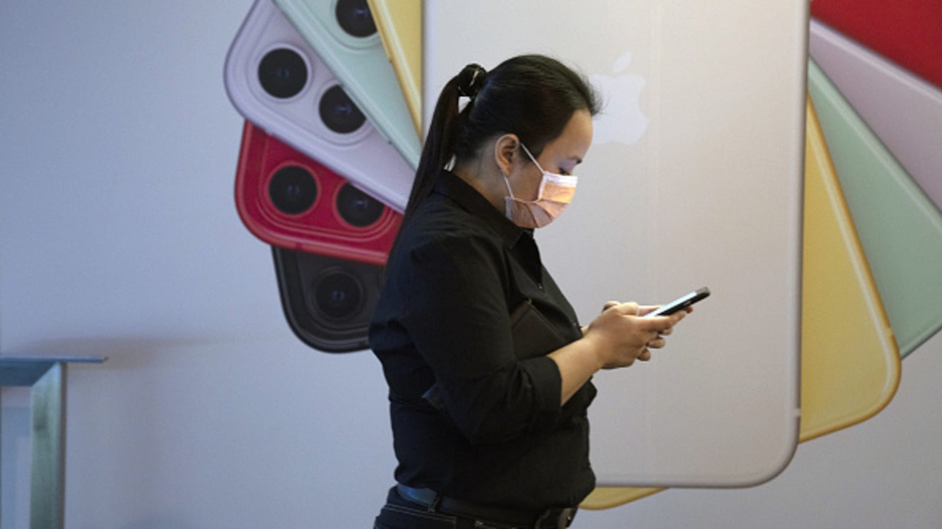 A pedestrian wearing a protective mask uses her mobile phone while walking past an Apple iPhone advertisement at Orchard Road in Singapore.