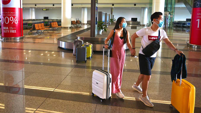 Passengers with protective face masks walk with their luggage in the empty arrival hall of Noi Bai International Airport in Hanoi, Vietnam.
