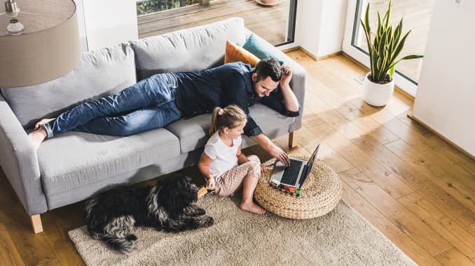 dad on couch working on laptop with daughter and pet dog