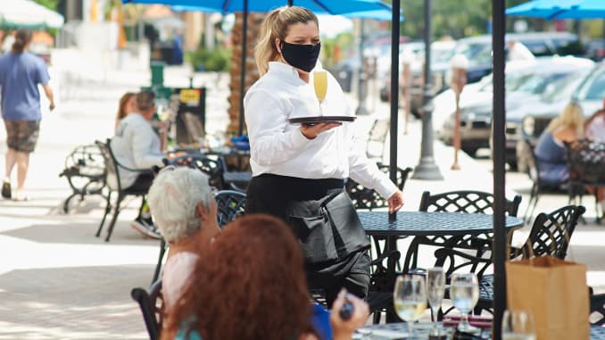 A server wearing a protective mask serves a drink to a customer in the outside dining area of a restaurant in St. Petersburg, Florida, on Monday, May 4, 2020.