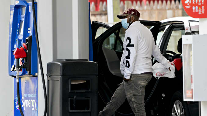 A customer wearing a protective mask uses a plastic shopping bag to hold a fuel nozzle while refueling a vehicle at an Exxon Mobil Corp. gas station in Arlington, Virginia.