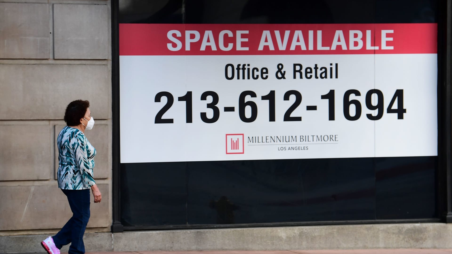 A woman wearing her facemask walks past advertising for office and retail space available in downtown Los Angeles, California on May 4, 2020.