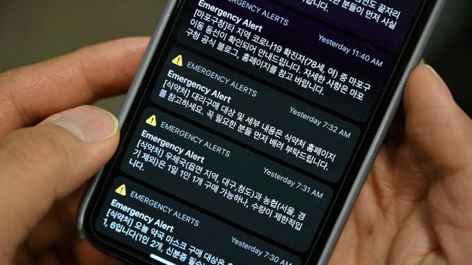 This photo illustration shows a man holding her phone showing emergency alert text messages announcing locations that confirmed COVID-19 patients have visited, among others, in Seoul on March 10, 2020.