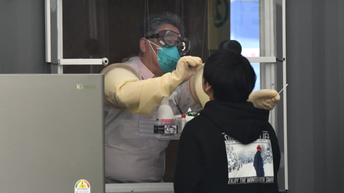 A medical staff member in a booth takes samples from a visitor for the COVID-19 coronavirus test at a walk-thru testing station set up at Jamsil Sports Complex in Seoul on April 3, 2020.