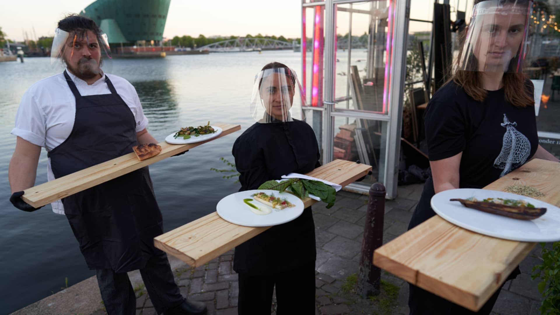 Waiters wear face shields and gloves and rely on long wooden boards to serve diners.